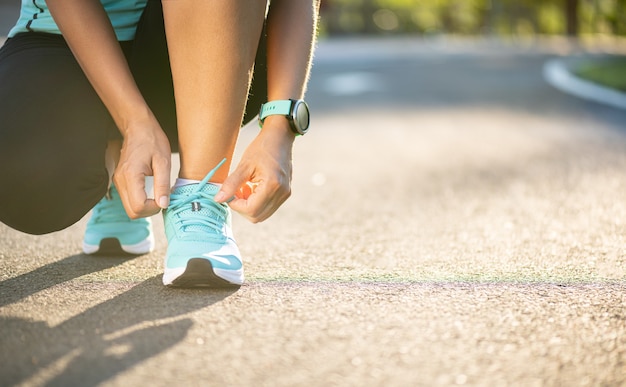 Running shoes - closeup of woman tying shoe laces. Female sport fitness runner getting ready for jogging in garden background.