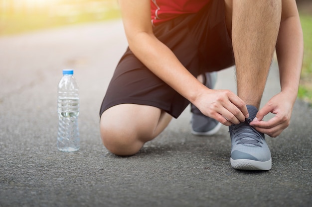 Running shoes - Man knee down with tie sneakers shoestring, Runner man getting ready for jogging at garden.