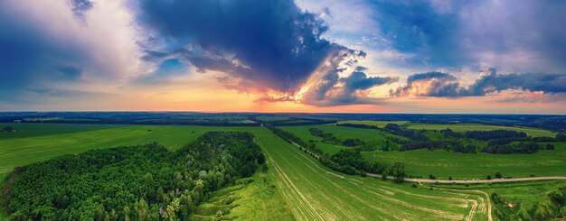 Rural summer sunset landscape with green fields and dramatic colorful sky natural background aerial view panorama