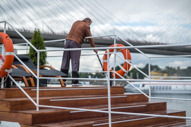 Russia St Petersburg September 10 2022 A man cleans the deck of a yacht with a hose