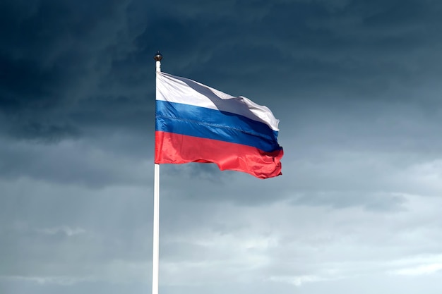 Russian flag on flagpole waving against dark gloomy rainy clouds on the sky