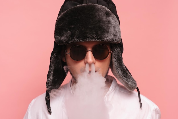 A Russian man in a traditional hat smokes a hookah and enjoys it Pink background