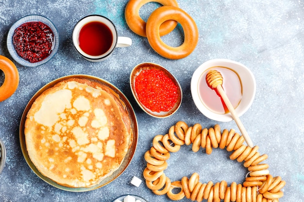 Russian pancake blini with raspberry jam, honey, fresh cream and red caviar, sugar cubes, cottage cheese, bubliks on dark