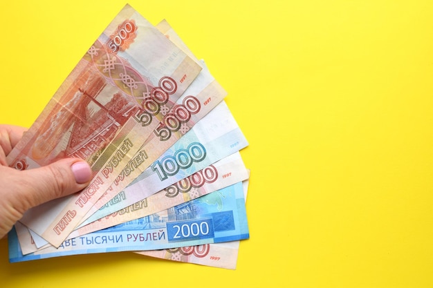 Russian ruble banknotes in a female hand on a yellow background Copy space