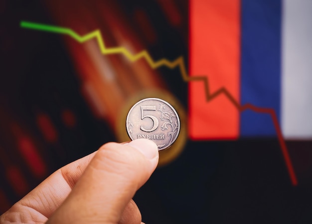 Russian ruble coin holding on the hand with falling down trading charts and russian flags background