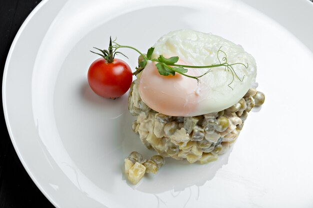 Russian salad Olivier served with poached egg on top