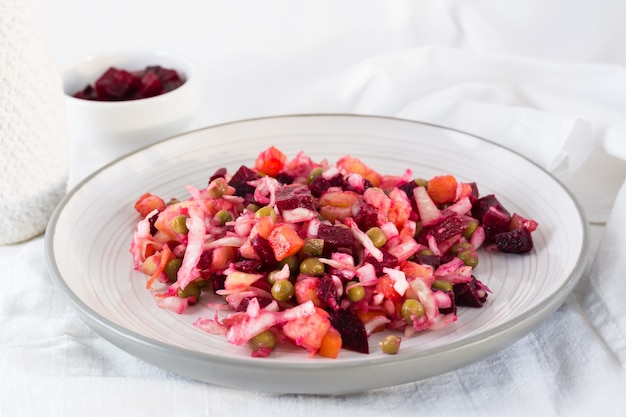 Russian traditional salad with vegetables - vinaigrette on a plate and a bowl of beets on a table on a cloth. Close-up