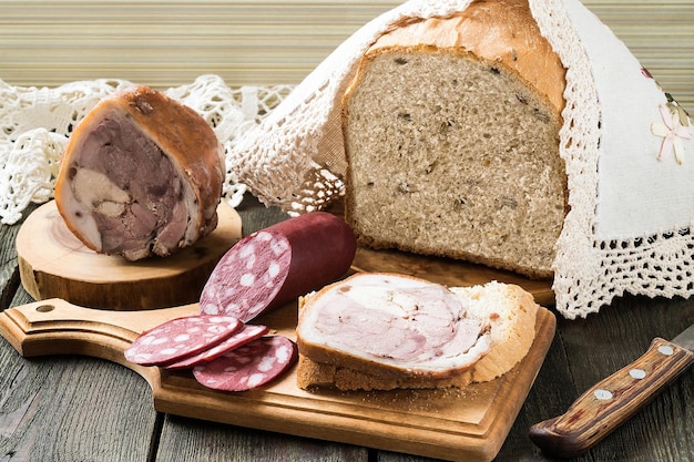 Russian wholegrain homemade wheat bread with sunflower seeds on the board under the cloth with knitted border and homemade meat products