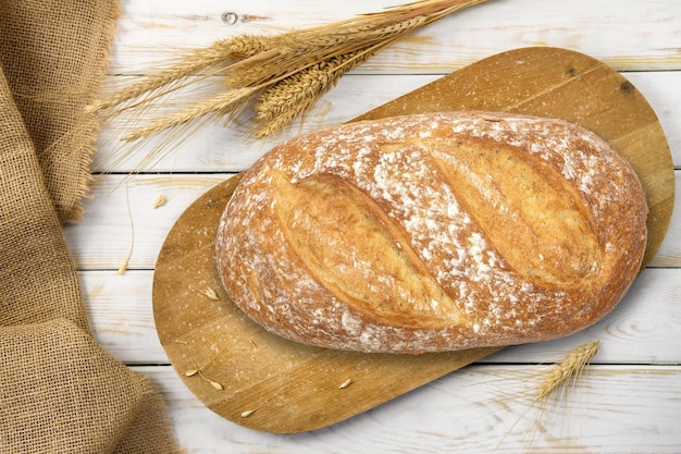 Rustic baking template top view of a fresh baked bread on a wooden vintage cutting board with cereal grains and burlap sack