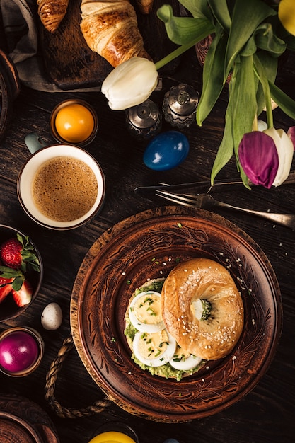 Rustic easter breakfast flat lay with eggs bagels, tulips, croissants, egg, oatmeal with berries, colored quail eggs and spring holidays decorations. Top view