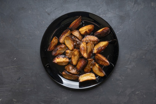 Rustic fried potatoes on a black dish on the table, top view