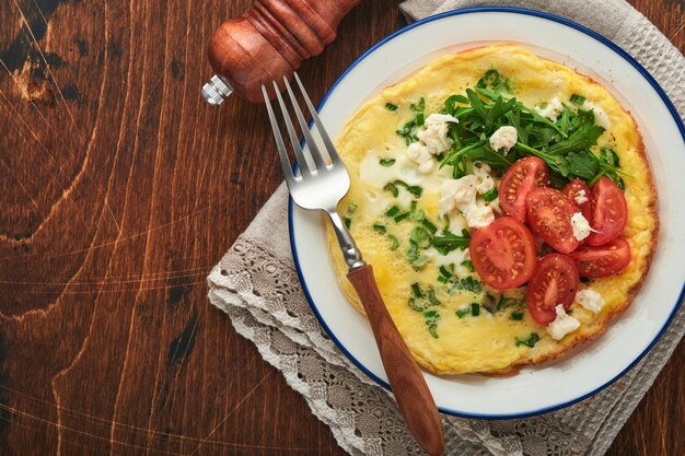 Rustic omelette or frittatas with green onions cheese mozzarella green arugula and tomatoes on old wooden dark background Healthy food concept Breakfast Copy space Top view Mock up