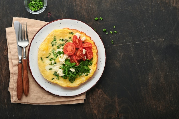 Rustic omelette or frittatas with green onions cheese mozzarella green arugula and tomatoes on old wooden dark background Healthy food concept Breakfast Copy space Top view Mock up