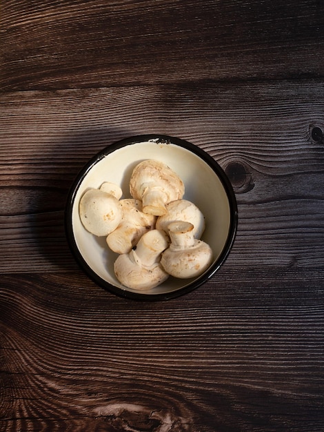 Rustic pewter container with raw mushrooms on dark wood