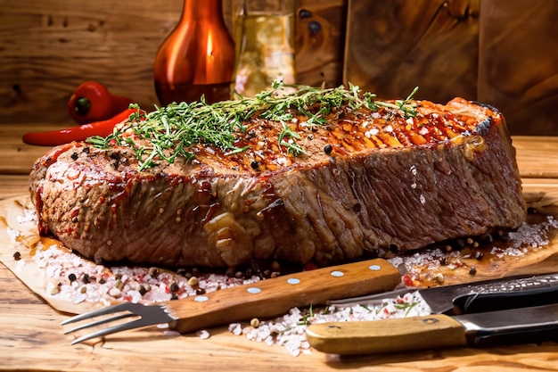 a rustic table with a large steak roasted with smoke spices herbs and rock salt pepers