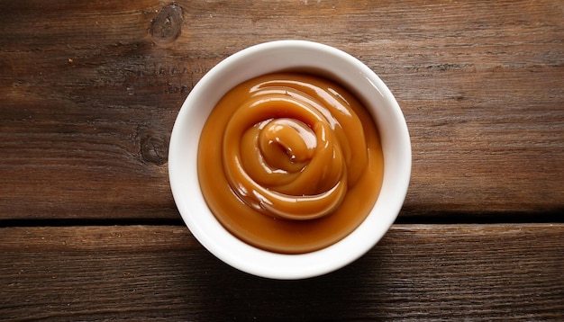 rustic wooden table displays a white bowl filled with smooth and creamy dulce de leche highlighting