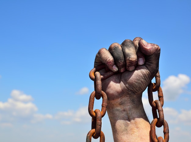 Rusty iron chain in human male right hand against the blue sky