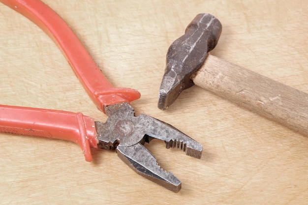 A rusty metal hammer with a wooden handle lies opposite a plier with a red plastic winding