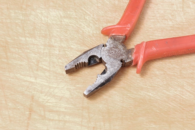 Rusty metal pliers with a red plastic handle lie at an angle on a lightcolored wooden board