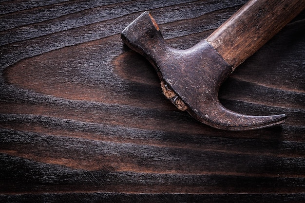 Rusty oldfashioned claw hammer on vintage dark wooden board close up view construction concept