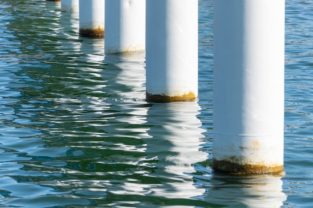 Photo rusty pier posts in salt sea water. white columns diagonal. pillars mount for bridge. sunny weather.