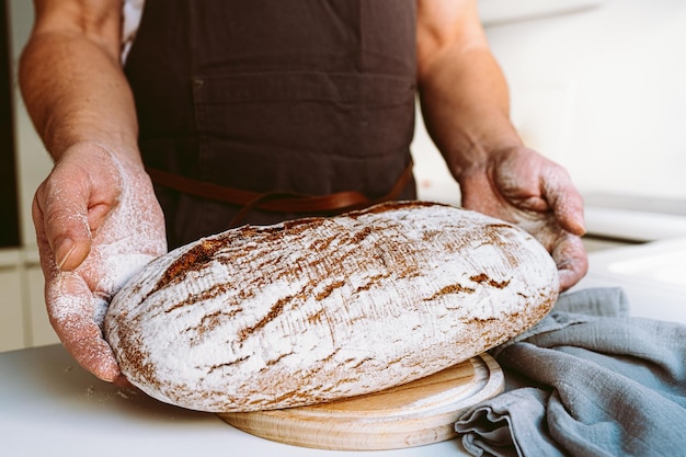 Rye craft homemade bread in muscular textured hands of male baker