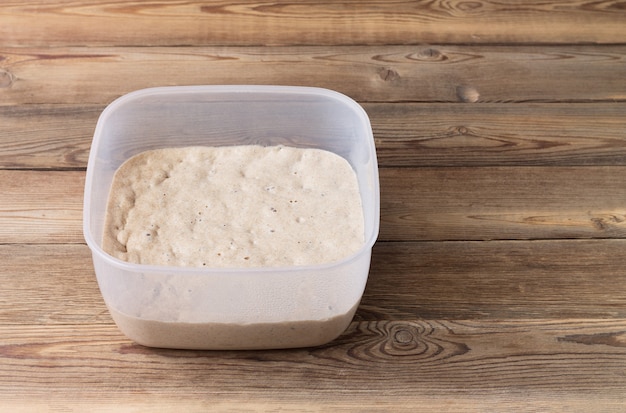 Rye sourdough on flour sourdough in a container on a wooden table. Fermentation. Image contains copy space.