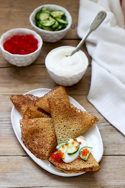 Rye and whole grain pancakes served with sour cream, caviar and cucumbers. Rustic style.