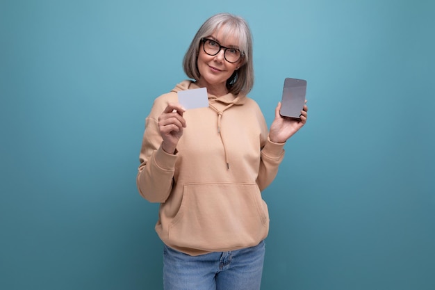 S granny woman with gray hair keeps her savings on a credit card on a studio background with copy