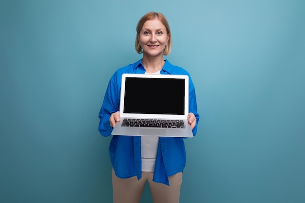 S middle aged business woman showing laptop screen with mockup on blue background with copy space