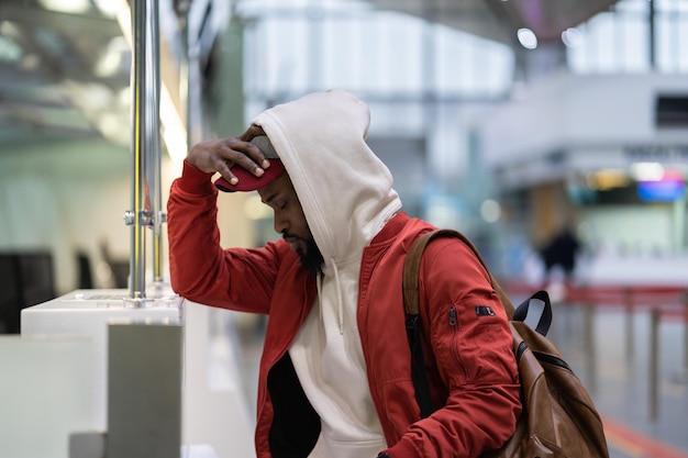 Sad african man standing near checkin desk feeling frustrated because of flight cancellation