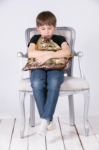 Sad boy sitting on a chair hugging a pillow