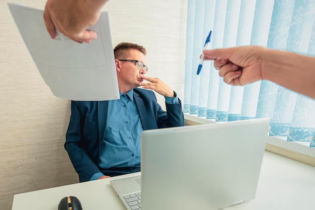 Sad businessman in a suit sits in the office and looks at the documents Conclusion of a contract with the boss Unwillingness to sign a contract Dismissal of an employee