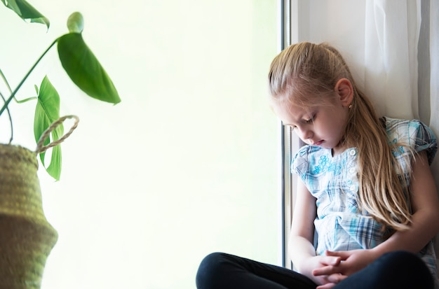 Sad child girl by the window