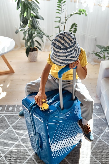 A sad child sits on a suitcase and waits for departure plays with a toy car family relocation flight