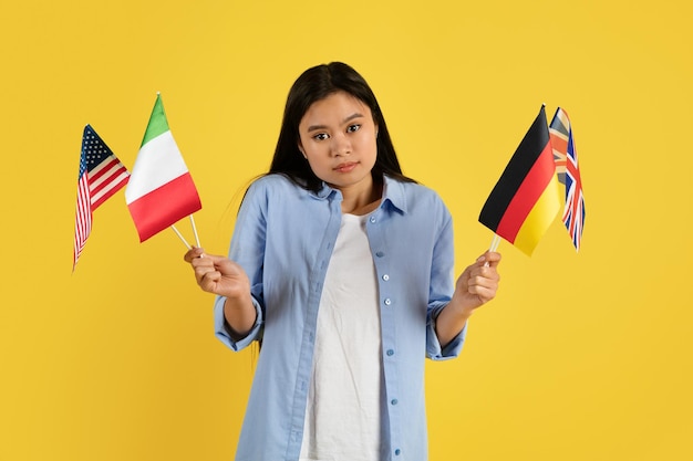 Sad confused young chinese female student in casual with many different flags look at camera