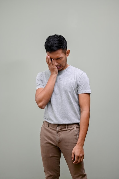 Sad and crying Asian man covering his face feeling upset and failing isolated background