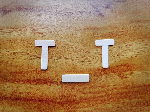 Photo sad and crying symbol using letters t and i on wooden table