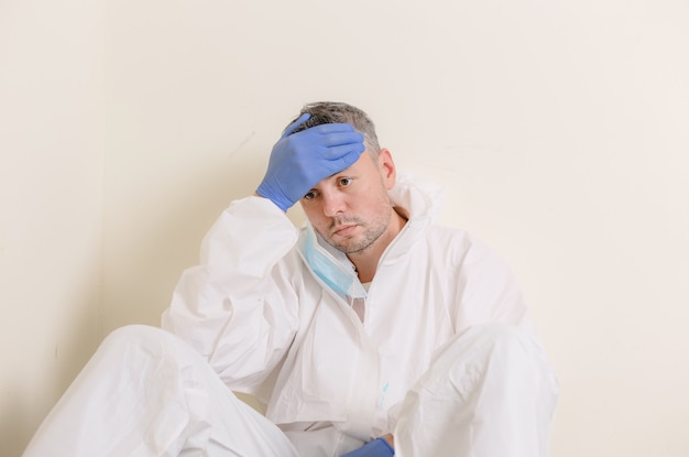 A sad doctor in a protective suit sits on the floor in the corridor of the hospital. Health workers during the Covid19 coronavirus pandemic.