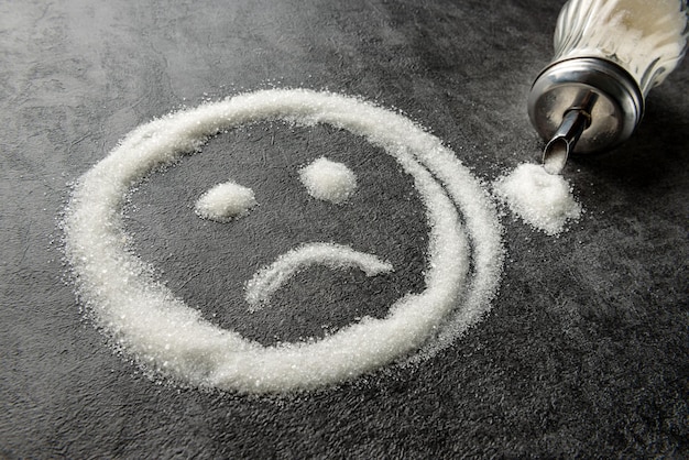 Sad emoticon drawn with sugar on the table