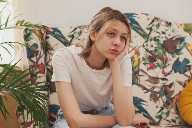 Sad emotion young woman is sit in waiting room wait for her turn. Female sitting on sofa feels apathy uncomfortable. Concept of long waiting in institution and hospital. Selective focus. Copy space