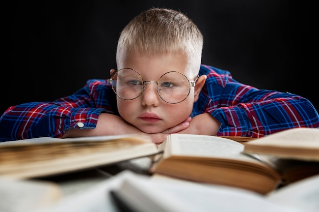 A sad fat boy with glasses sits with books at the table. Education and knowledge. Close-up.