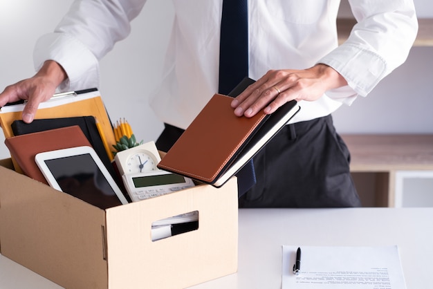 Sad Fired Young Employee businessmen hold boxes including pot plant and documents for personal belongings unemployment, resigned concept.