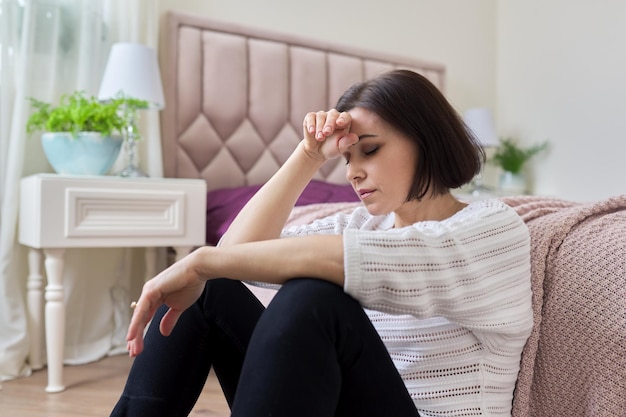 Sad frustrated depressed mature woman sitting at home on the floor