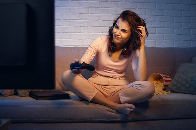 Sad gamer girl playing video games on the console in her apartment