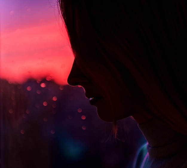 Sad girl by the window against the sunset with rain