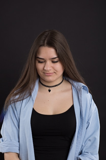 Sad girl in denim shirt with long hair, on black wall