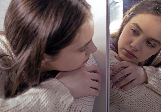 Sad girl in depression looks at her reflection in the mirror