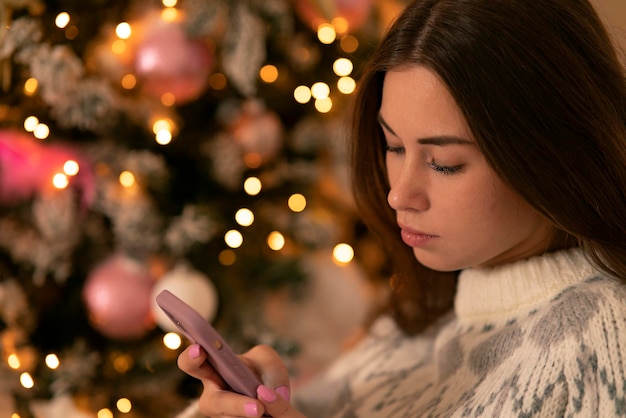 Sad girl holding a mobile phone against the background of a festive christmas tree woman with smartp...