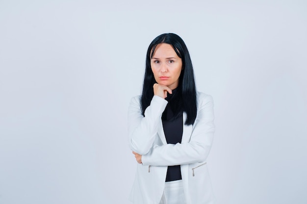 Sad girl is looking at camera by putting hand under chin on white background